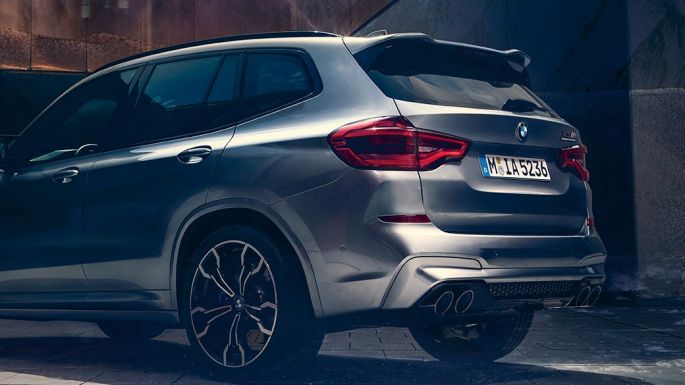 BMW X3 M Competition, vue de profil arrière. Extérieur de la BMW X3 M Competition en Donington Grau metallic, vue de profil arrière avec deux personnes à l'avant-plan.