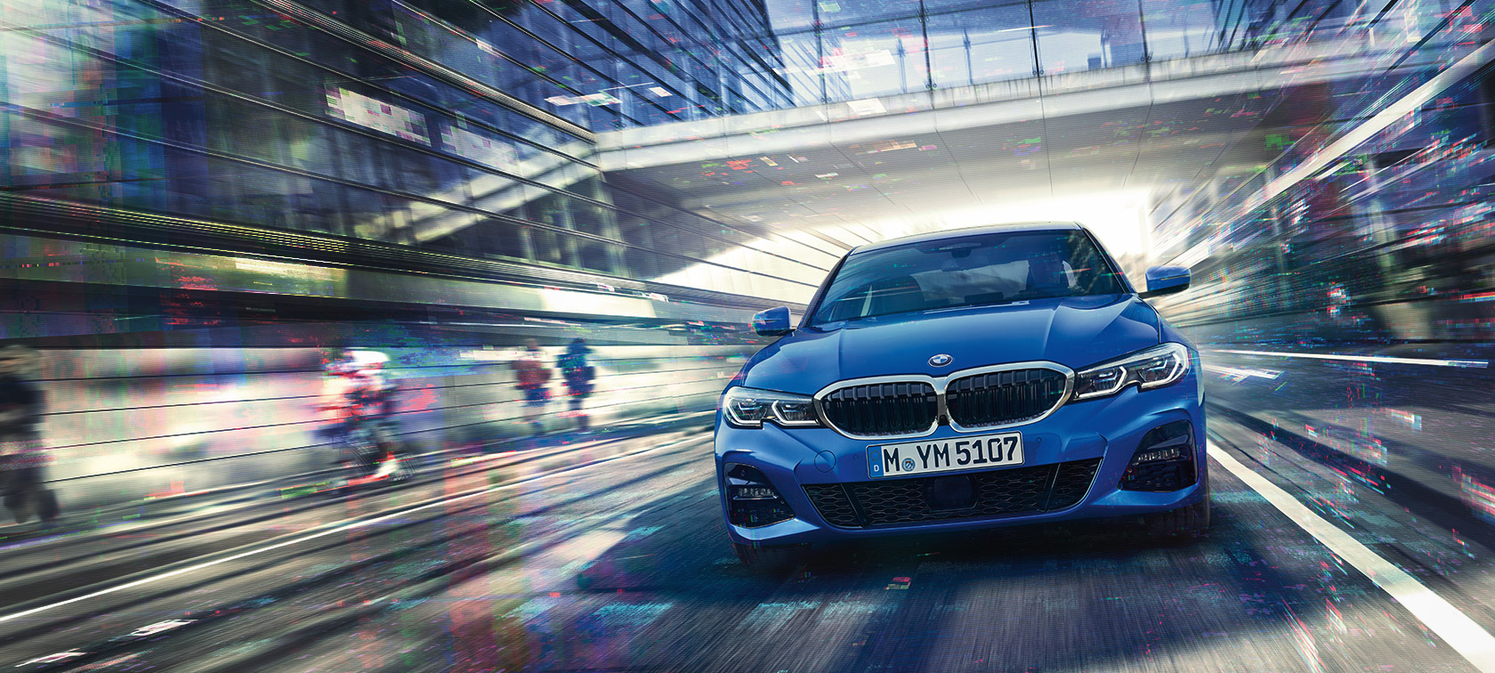 Vue de face de la BMW Série 3 Berline (G20) roulant de jour en bas d’immeubles en verre.