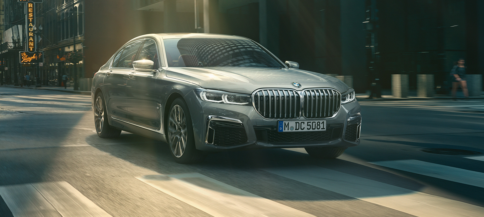 Vue de trois quarts avant d’une BMW Série 7 Berline grise en mouvement Vue de trois quarts avant d’une BMW Série 7 Berline grise roulant dans un décor urbain