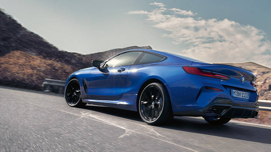 La nouvelle BMW Série 8 Coupé G15 LCI restylage vue de trois quarts arrière en mouvement La nouvelle BMW Série 8 Coupé M Portimao Blau metallic G15 LCI restylage vue de trois quarts arrière face aux collines