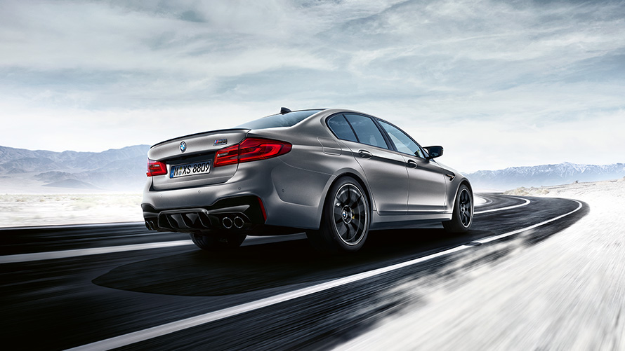 M5 Competition grise en vue arrière de biais sur autoroute face à un paysage désertique