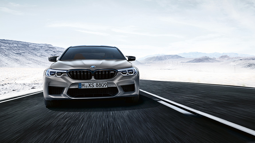 M5 Competition grise vue de face de biais sur autoroute face à un paysage désertique