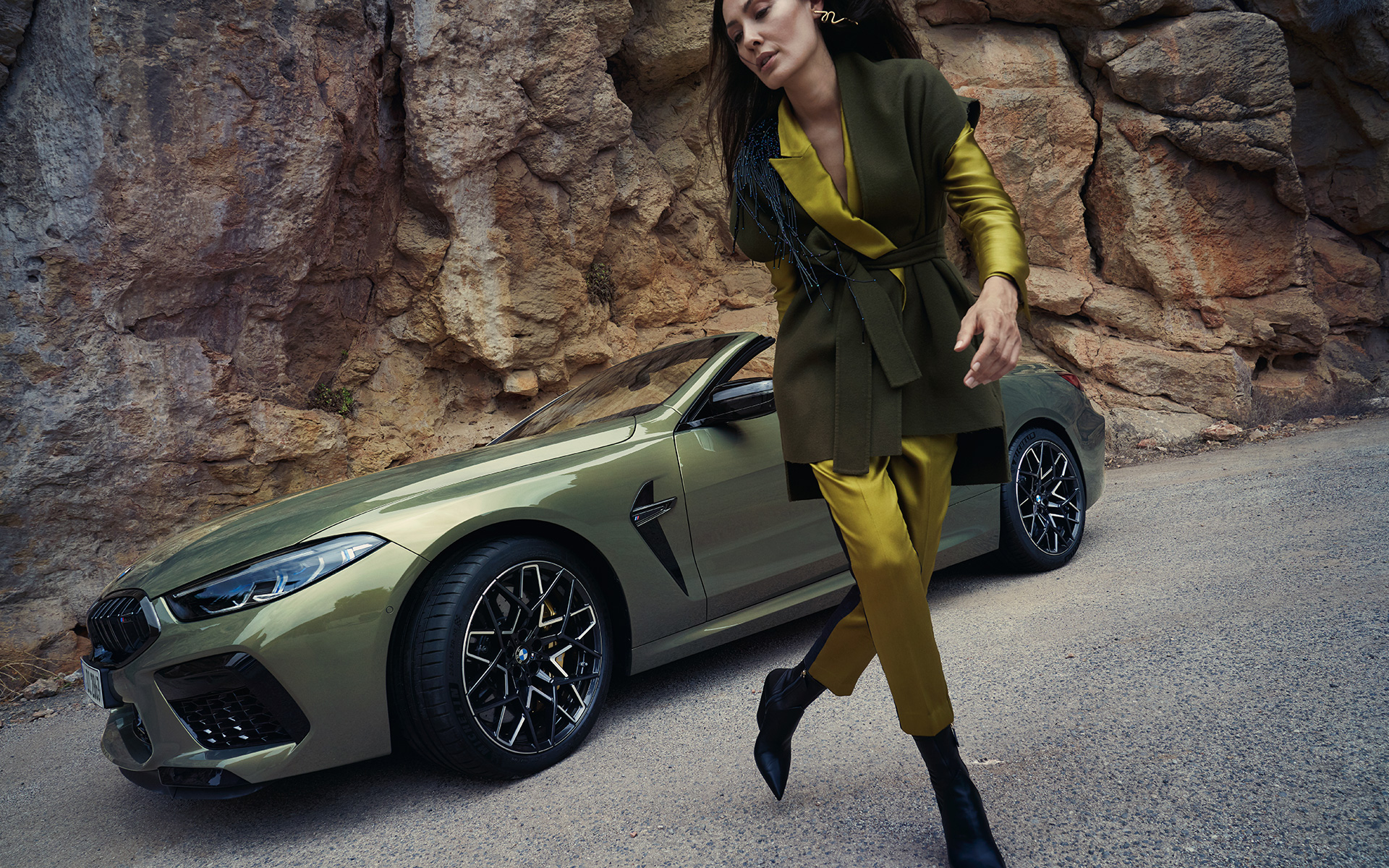 La nouvelle BMW M8 Competition Cabrio F91 LCI 2022 vue de trois quarts avant sur un terrain rocailleux La nouvelle BMW M8 Competition Cabrio F91 LCI restylage 2022 BMW Individual Brass metallic vue de trois quarts avant sur un terrain rocailleux avec mannequin féminin