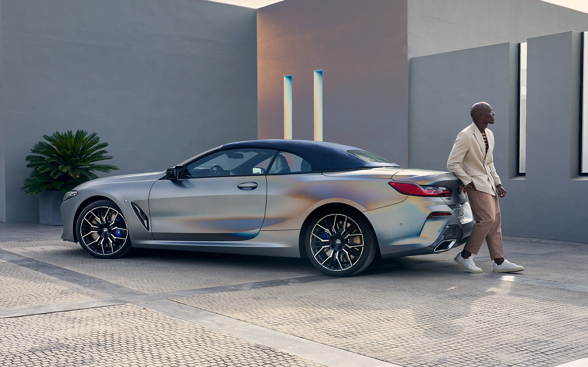 Vue de trois quarts arrière de la nouvelle BMW M850i xDrive Cabrio G14 LCI restylage 2022 La nouvelle BMW M850i xDrive Cabrio G14 LCI restylage 2022 BMW Individual Frozen Pure Grey metallic, vue de trois quarts arrière adossée au véhicule avec un modèle homme