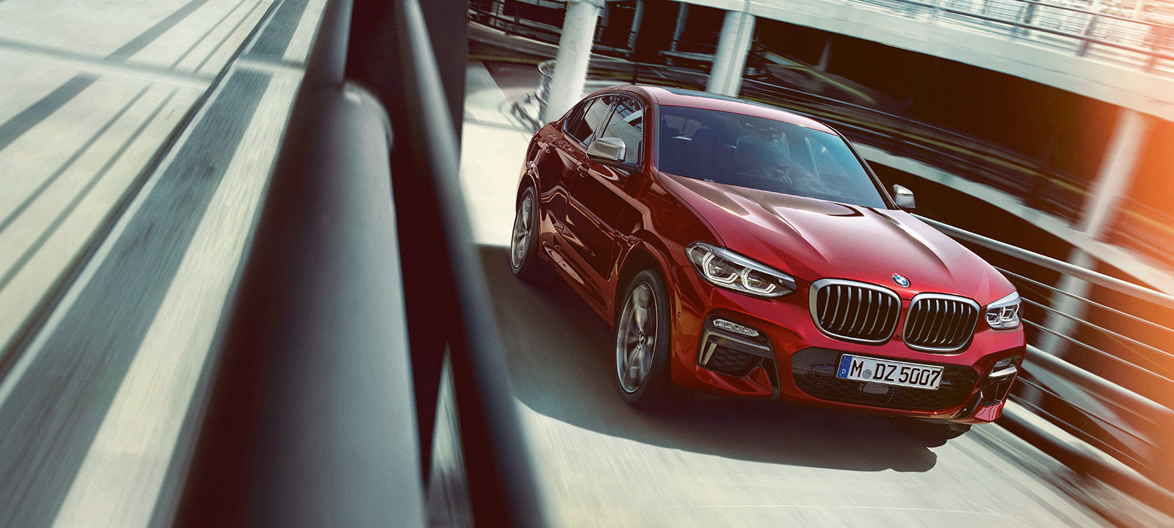BMW X4 entrant dans un parking couvert BMW X4 G02 2018 en Flamencorot Brillanteffekt, vue de trois quarts arrière, sortant d’un parking couvert